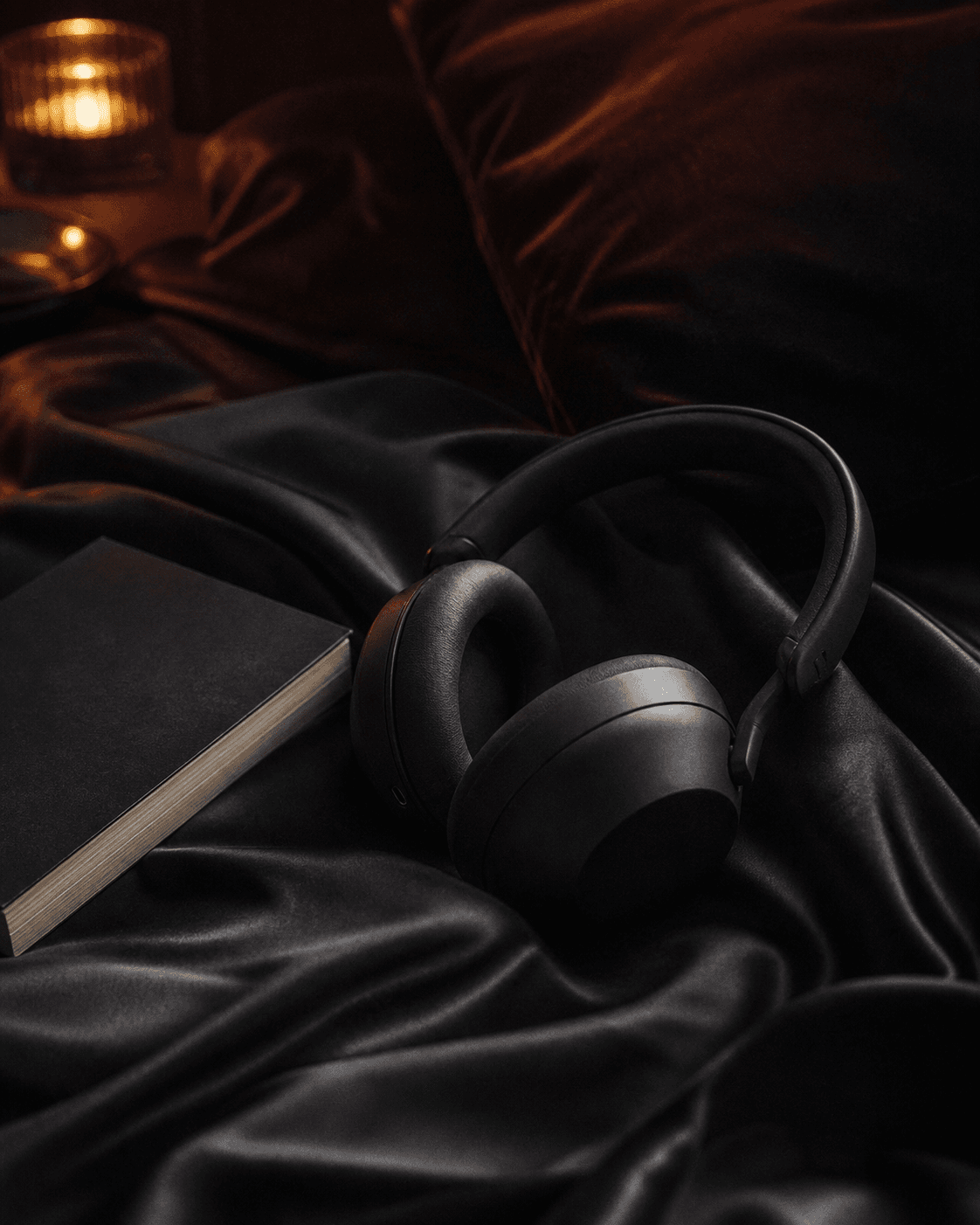Black headphones on dark satin beside a closed book